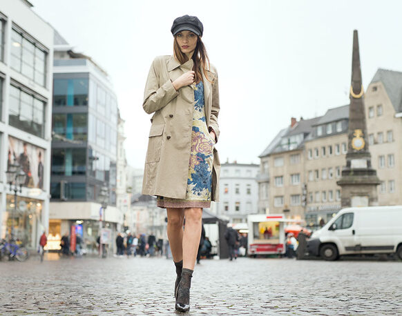 Weibliches Model mit Trenchcoat und Kappe geht über den Bonner Marktplatz.