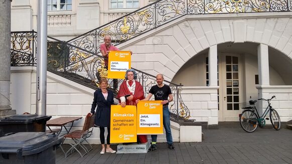 Drei Personen stehen mit Plakaten von GermanZero an der Beethovenfigur vor dem Alten Rathaus