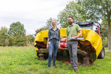 Zwei Personen auf einer Wiese vor einer Mähmaschine