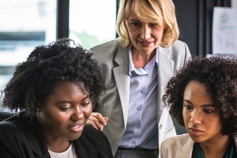 Drei Frauen besprechen sich und schauen zusammen auf einen Laptop.