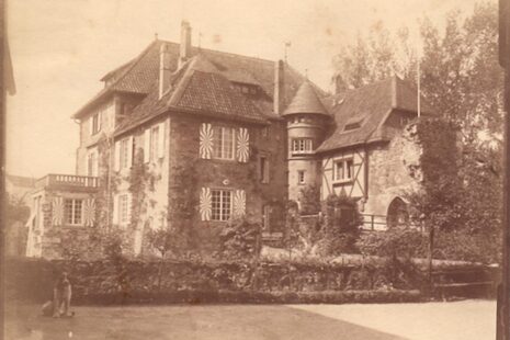 Zdjęcie przedstawia zamek Lede około 1900 roku na starej fotografii w sepii. Widoczna jest architektura z wieżyczką umieszczoną między dwoma bokami budynku, wykusz z balkonem powyżej, brama zamkowa i okiennice.