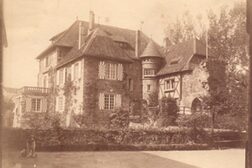 Das Foto zeigt die Burg Lede um 1900 auf einem alten Sepia-Foto. Es ist eine Architektur mit einem Türmchen zwischen zwei Seiten des Gebäudes platziert, es gibt einen Erker mir darüberliegendem Balkon, ein Burgtor und Fensterläden.