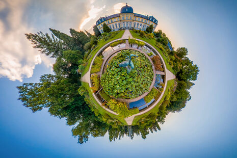 La photo montre le château de Poppelsdorf et une partie du parc sur un fond de ciel bleu. On a l'impression qu'il s'agit d'une sphère qui flotte dans le ciel, comme la Terre dans l'espace.